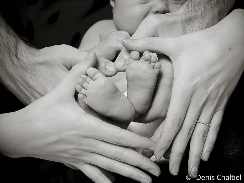 Photo en noir et blanc de parents tenant leurs mains en forme de coeur autour des pieds de leur bébé.